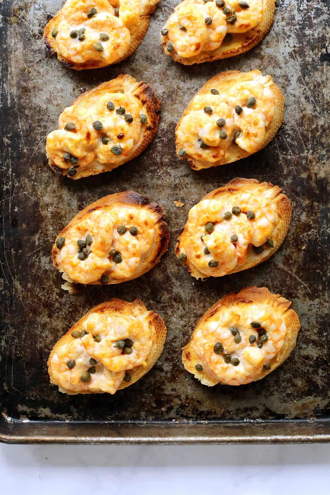 Sriracha garlic shrimp toast is made with tender shrimp, spicy sriracha mayo, and lightly crispy toast! An easy appetizer or light meal. Sriracha shrimp toast on a baking sheet.