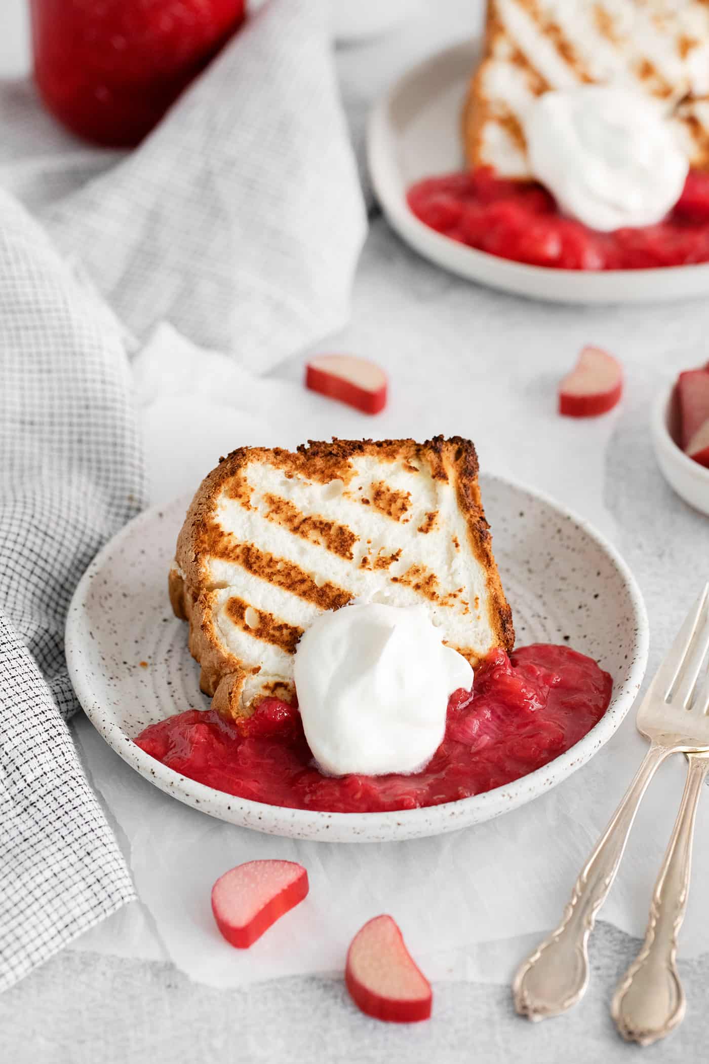 Grilled Angel Food Cake is a quick and easy way to elevate a simple angel food cake. Top with a sweet-tart rhubarb sauce and whipped cream, A slice of grilled angel food cake on a plate