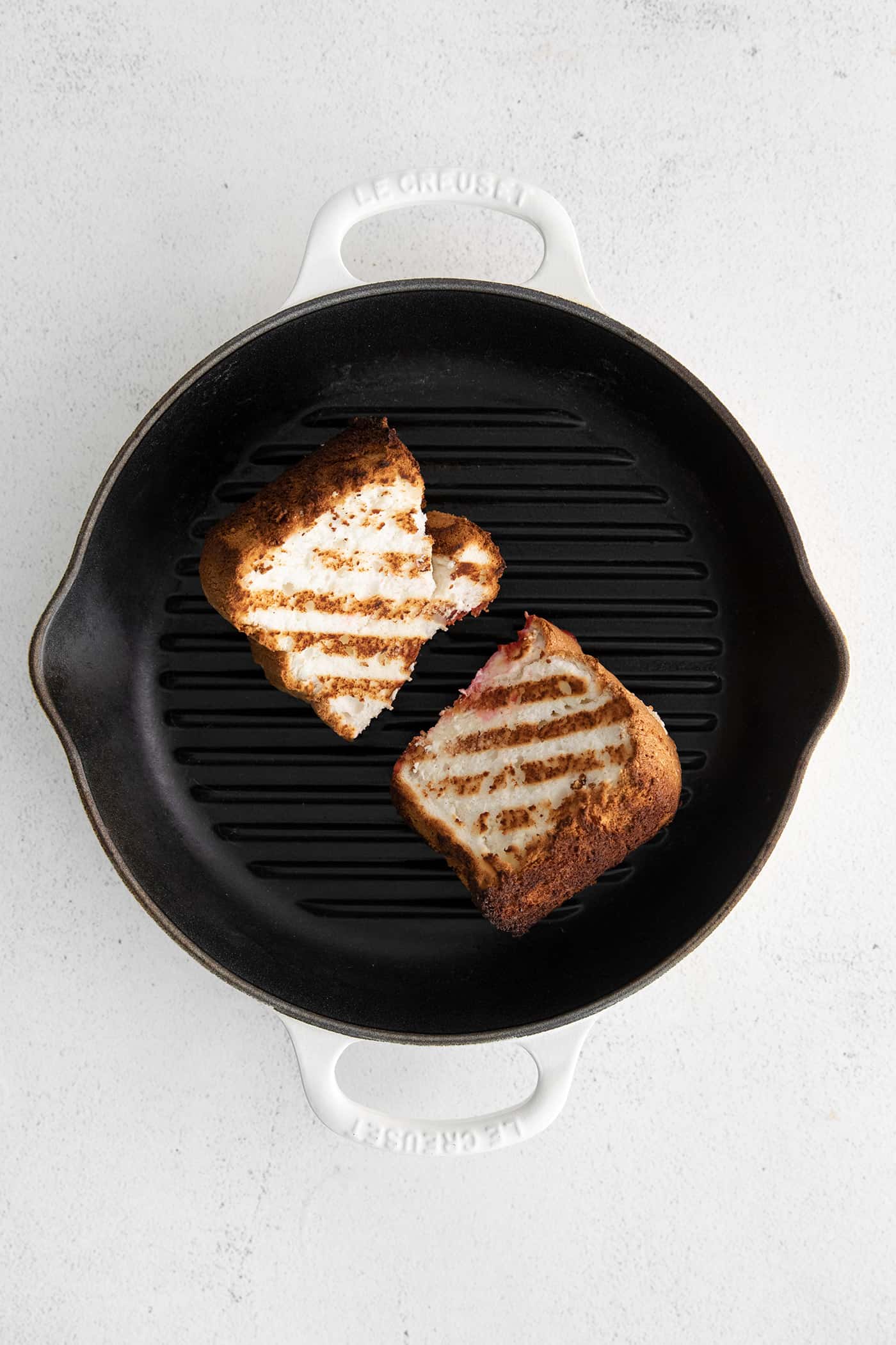 Grilled Angel Food Cake is a quick and easy way to elevate a simple angel food cake. Top with a sweet-tart rhubarb sauce and whipped cream, Two slices of angel food cake on a grill pan