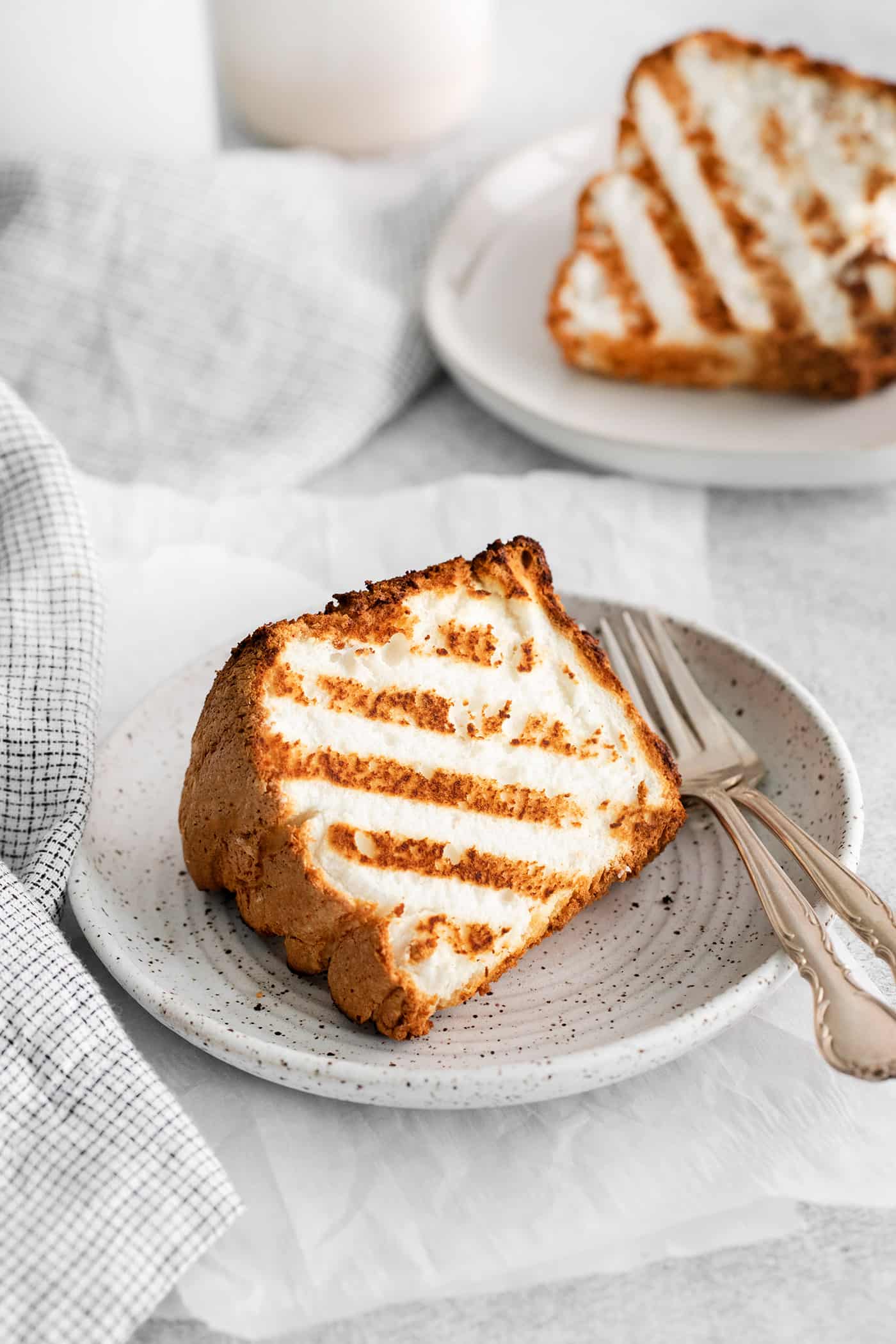 Grilled Angel Food Cake is a quick and easy way to elevate a simple angel food cake. Top with a sweet-tart rhubarb sauce and whipped cream, A slice of angel food cake on a plate