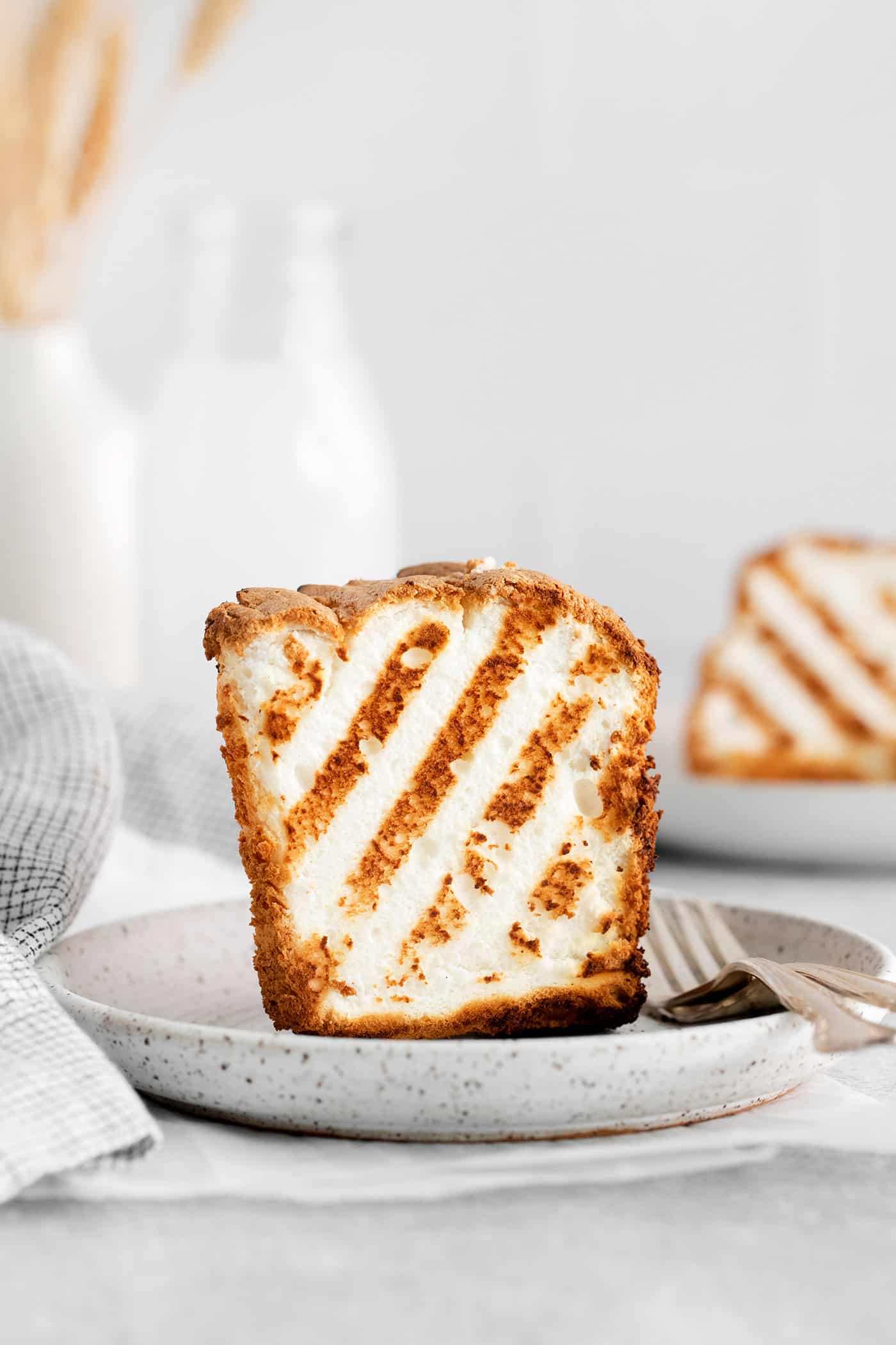 Grilled Angel Food Cake is a quick and easy way to elevate a simple angel food cake. Top with a sweet-tart rhubarb sauce and whipped cream, A slice of angel food standing up on a plate
