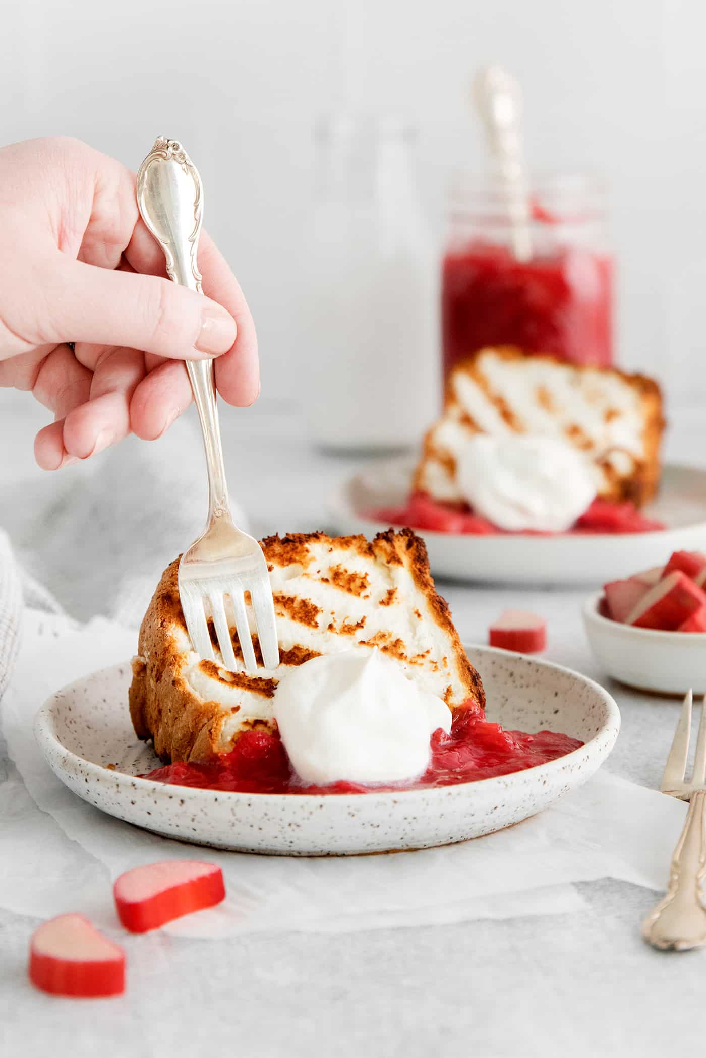 Grilled Angel Food Cake is a quick and easy way to elevate a simple angel food cake. Top with a sweet-tart rhubarb sauce and whipped cream, A fork diving into a slice of angel food cake with rhubarb sauce