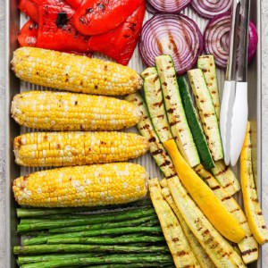 Closeup overhead view of grilled vegetables on pan with tongs
