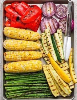 Overhead view of grilled vegetables on sheet pan with tongs