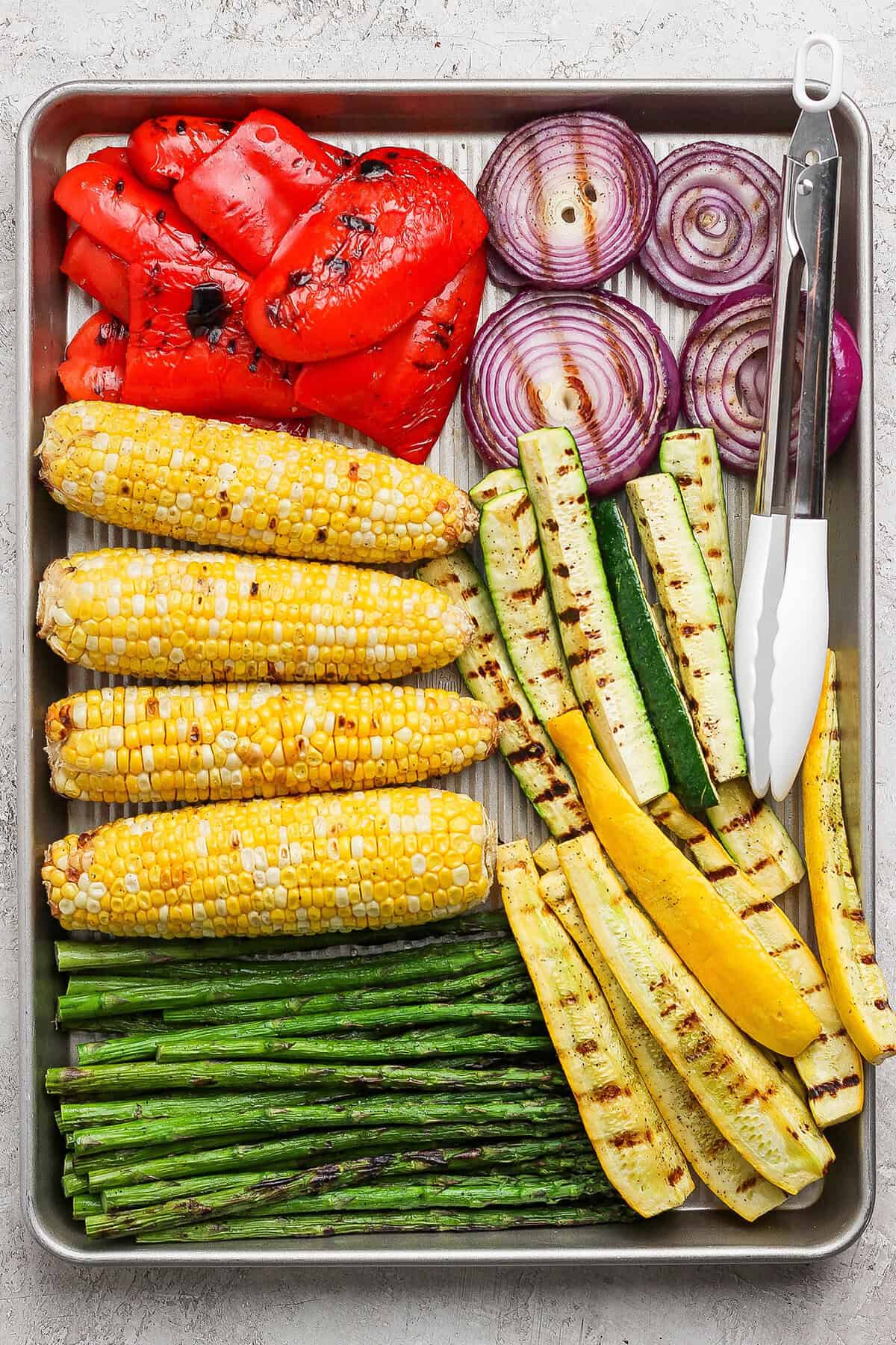 Overhead view of grilled vegetables on sheet pan with tongs
