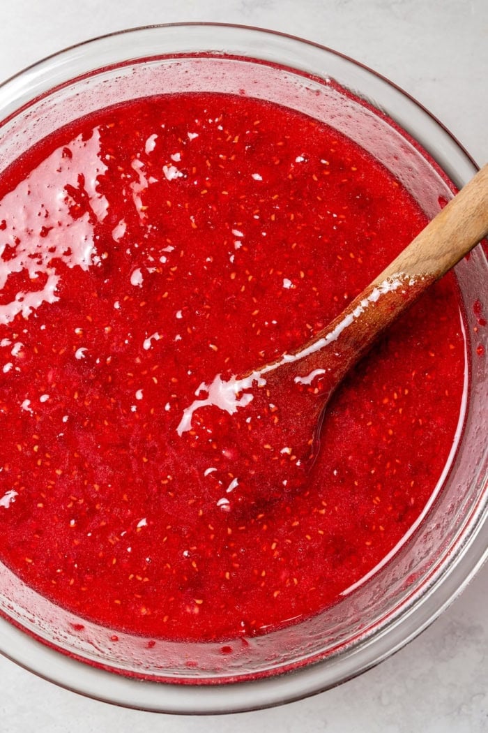This Raspberry Freezer Jam is the easiest you'll ever make—no canning needed! It's a delicious way to extended the life of your berries. Wooden spoon in bowl of raspberry freezer jam