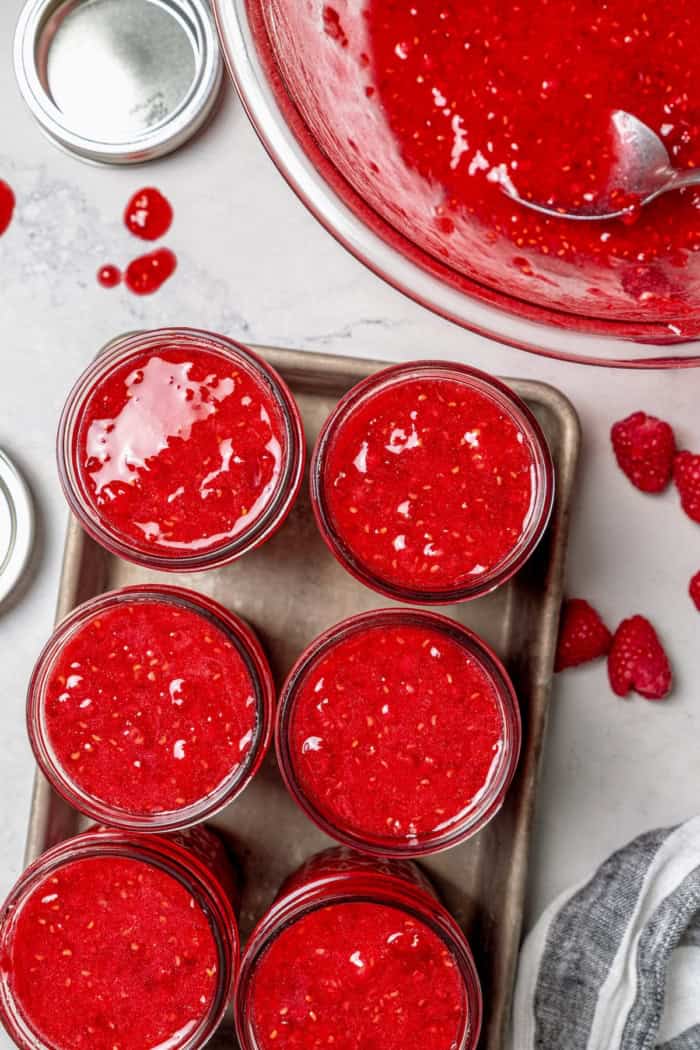This Raspberry Freezer Jam is the easiest you'll ever make—no canning needed! It's a delicious way to extended the life of your berries. Overhead view of 6 jars filled with raspberry freezer jam