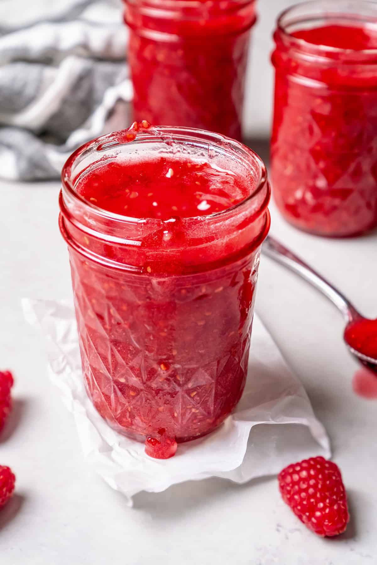 This Raspberry Freezer Jam is the easiest you'll ever make—no canning needed! It's a delicious way to extended the life of your berries. Open jar of raspberry freezer jam, with additional jars in background