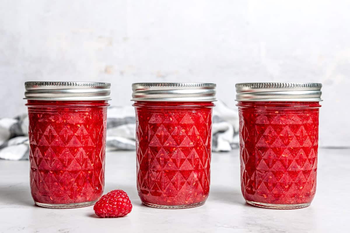 This Raspberry Freezer Jam is the easiest you'll ever make—no canning needed! It's a delicious way to extended the life of your berries. 3 jars of raspberry freezer jam on countertop