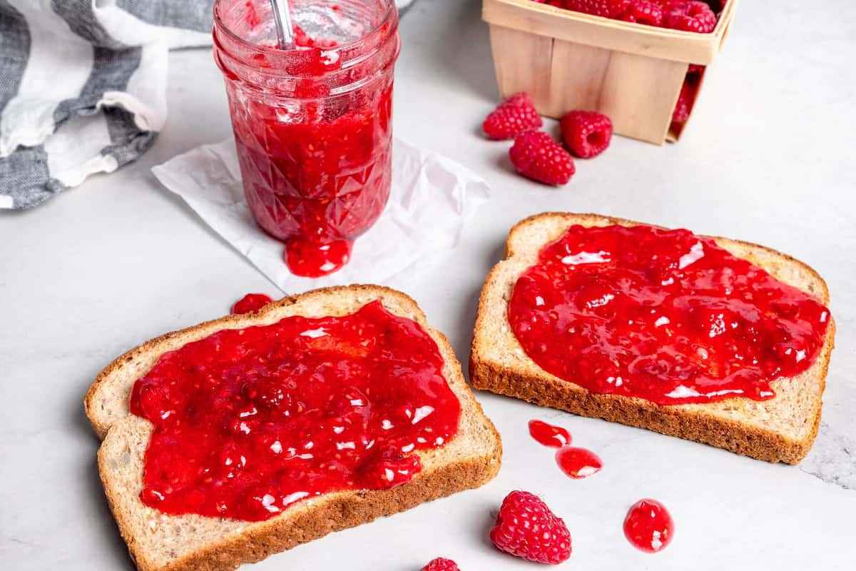 This Raspberry Freezer Jam is the easiest you'll ever make—no canning needed! It's a delicious way to extended the life of your berries. Two slices of jam with raspberry freezer jam