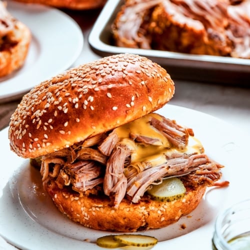 Slow cooker pulled pork sandwich with pickles and sauce.