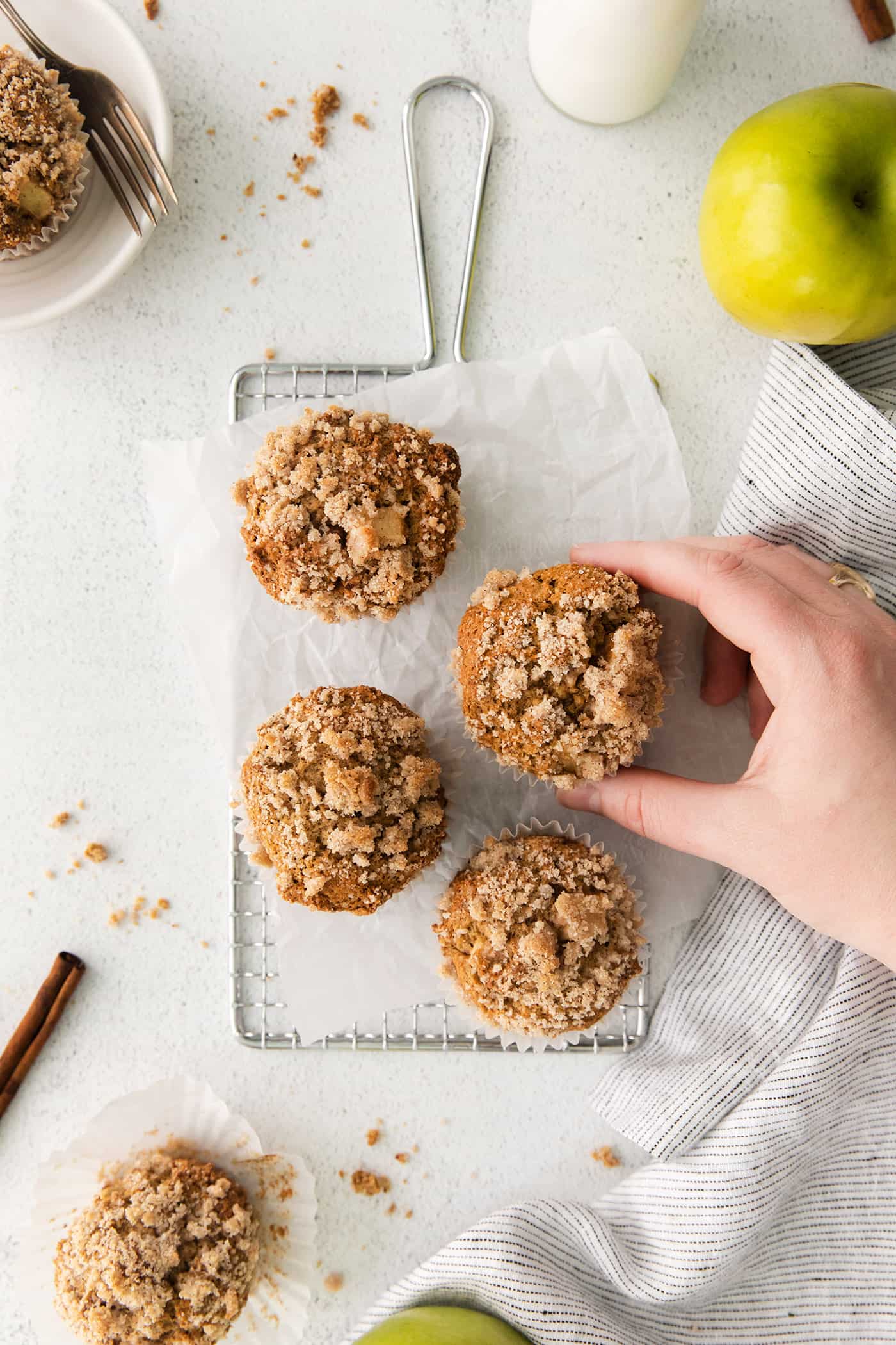 Make moist, tender apple muffins studded with juicy apple bites! Topped with cinnamon streusel, these easy muffins are great for fall baking. A hand reaching for an apple muffin