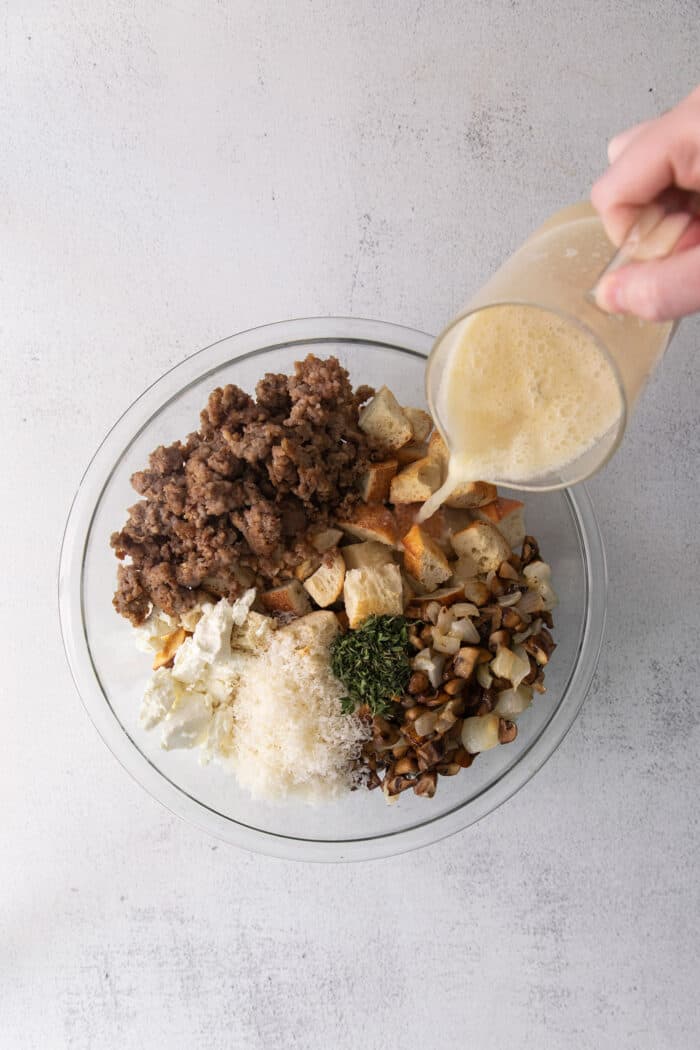This savory dressing with mushrooms, pork sausage, crispy garlic breadcrumbs, and Parmesan is the best Thanksgiving stuffing recipe! Broth being added to mushroom sausage dressing ingredients.