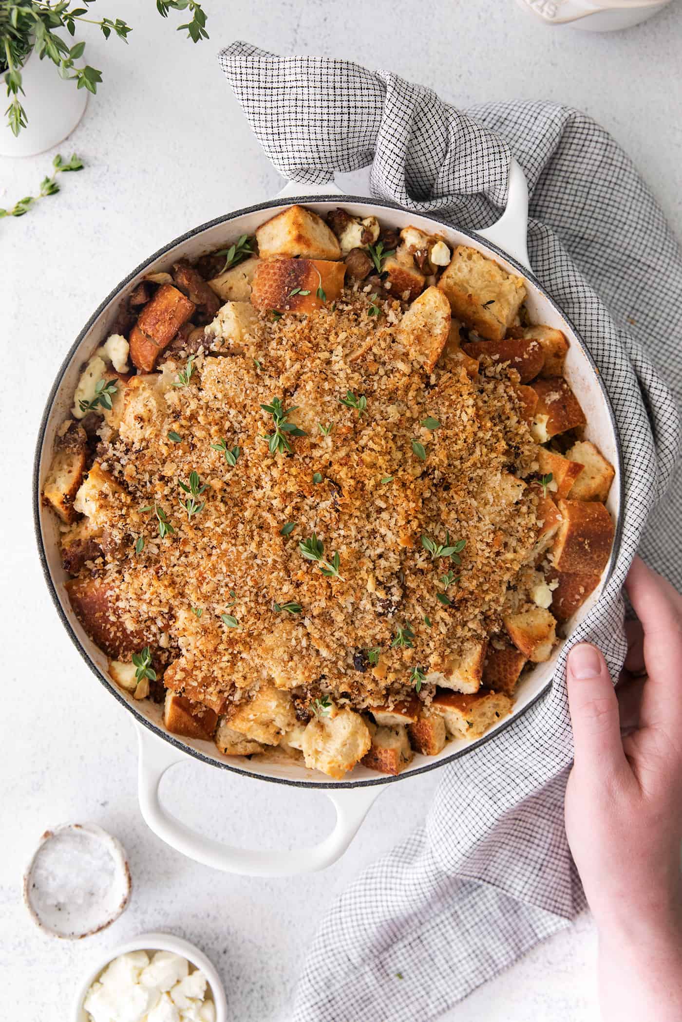 This savory dressing with mushrooms, pork sausage, crispy garlic breadcrumbs, and Parmesan is the best Thanksgiving stuffing recipe! Overhead view of a hand holding the side of a casserole dish with mushroom sausage dressing.