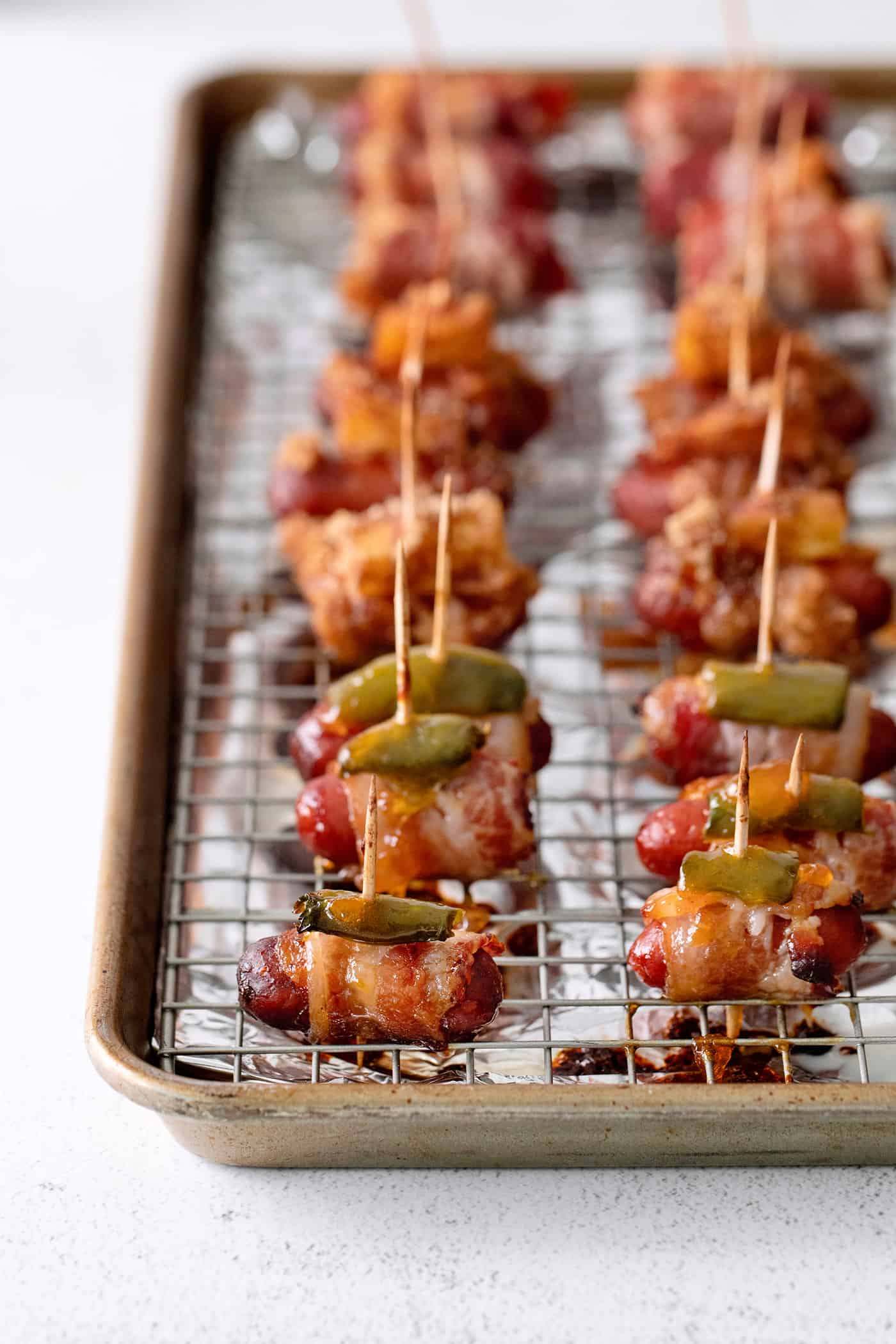 These Bacon Wrapped Smokies are the perfect game day appetizer. Switch things up by adding pineapple or jalapeno slices! Angled view of bacon wrapped weiners on a baking sheet