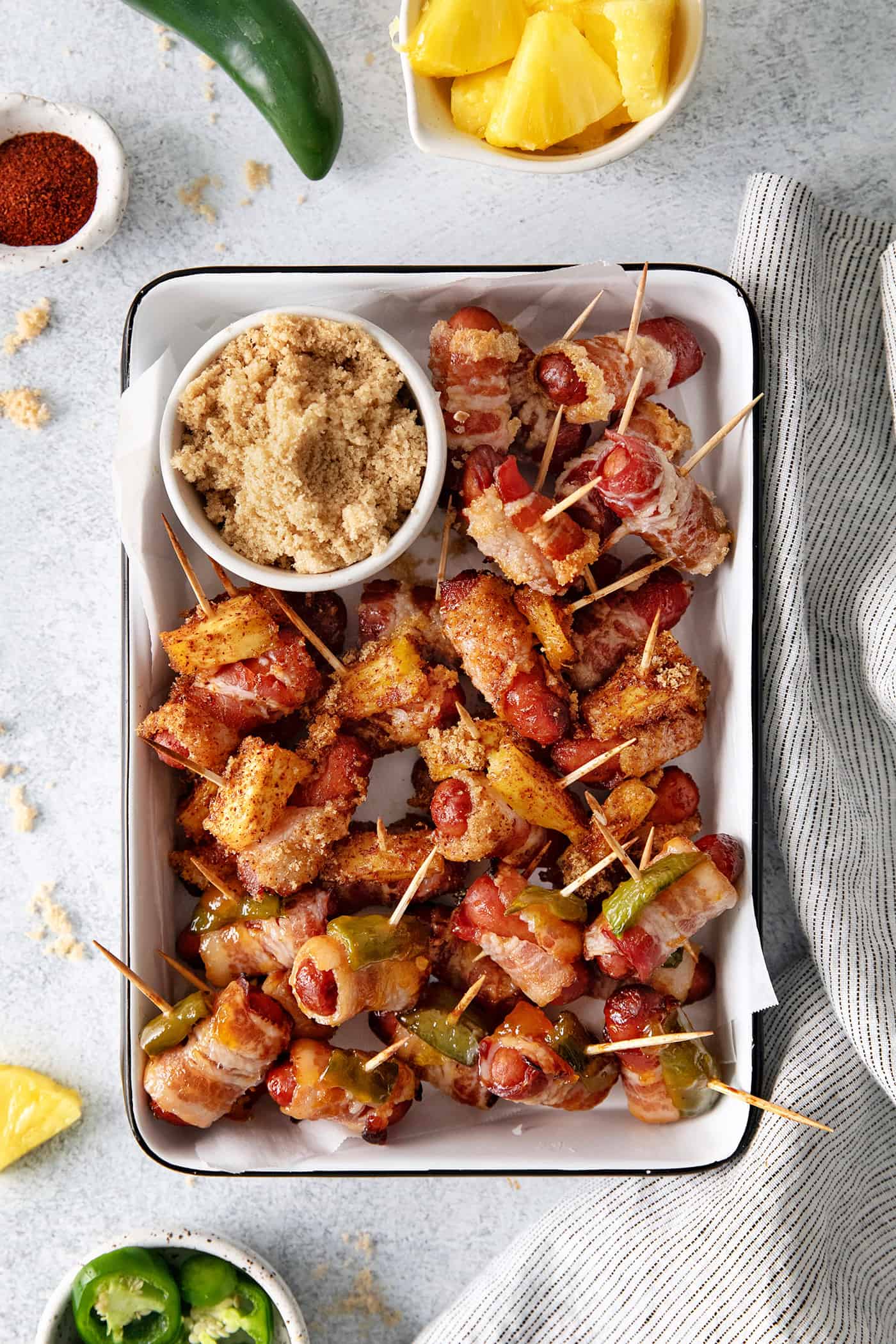 These Bacon Wrapped Smokies are the perfect game day appetizer. Switch things up by adding pineapple or jalapeno slices! Overhead view of bacon wrapped little smokies on a serving platter with a bowl of brown sugar