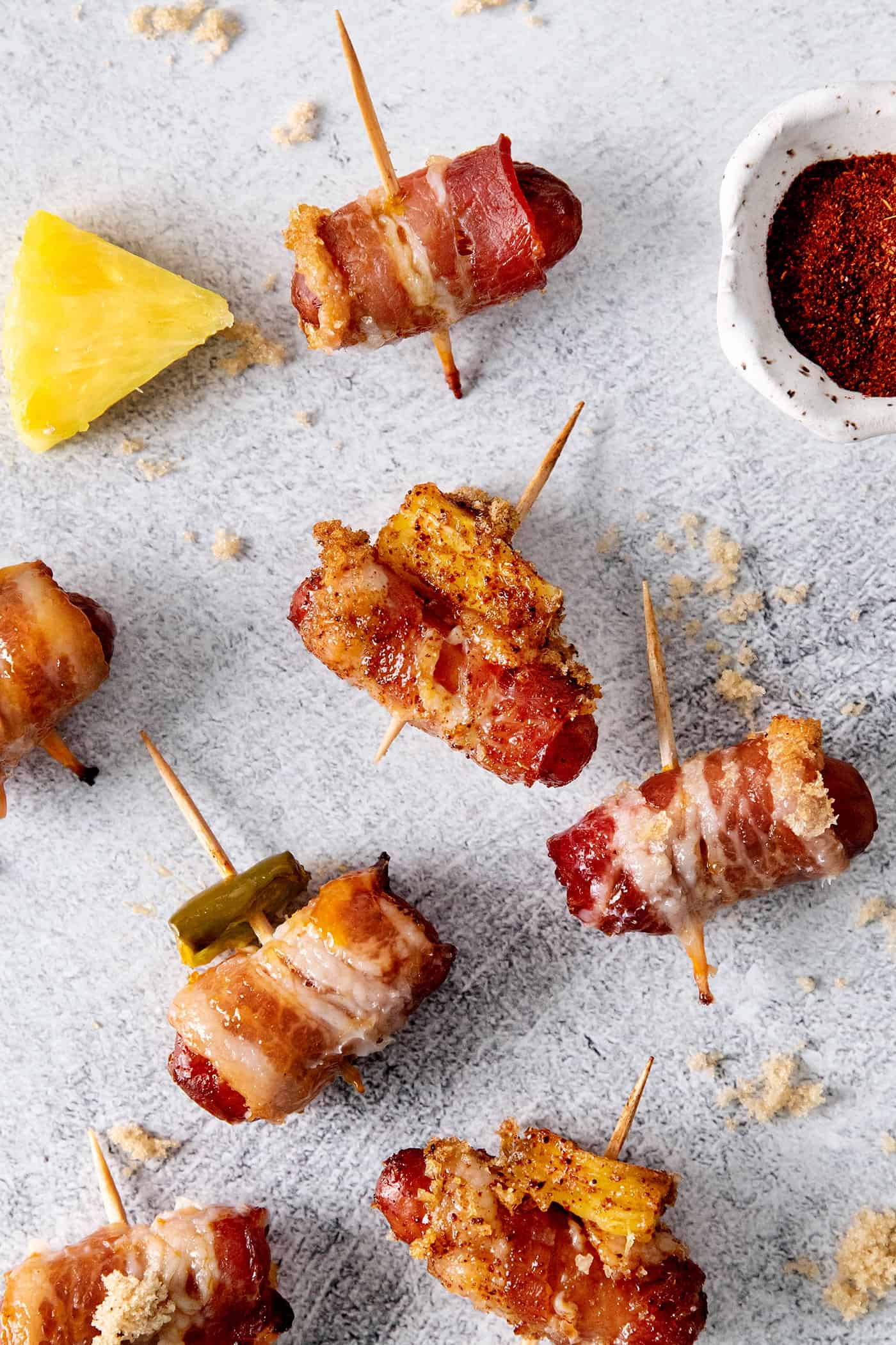 These Bacon Wrapped Smokies are the perfect game day appetizer. Switch things up by adding pineapple or jalapeno slices! Overhead view of 3 little smokies wrapped in bacon, one with pineapple and one with jalapeno