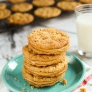 Chewy peanut butter sandwich cookies stacked on a green plate with peanut butter cookies on a wire rack and a glass of milk in the background.