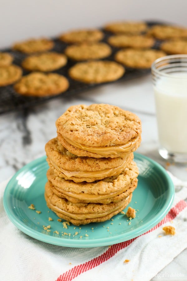 Peanut butter sandwich cookies combine soft, chewy peanut butter cookies with a rich and creamy filling, for double the flavor in every bite! Chewy peanut butter sandwich cookies stacked on a green plate with peanut butter cookies on a wire rack and a glass of milk in the background.