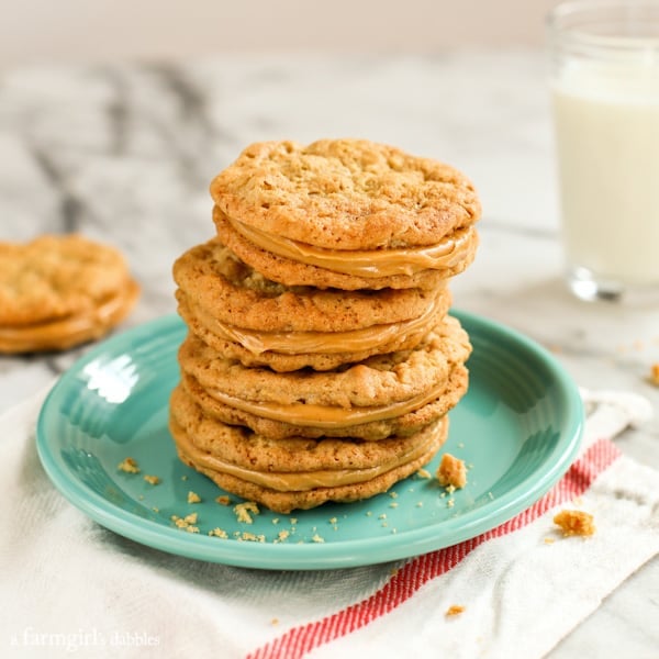 Buttery homemade peanut butter sandwich cookies stacked on a green plate with another cookie and a glass of milk in the background.