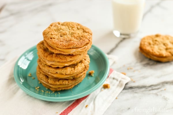 Peanut butter sandwich cookies combine soft, chewy peanut butter cookies with a rich and creamy filling, for double the flavor in every bite! Homemade peanut butter sandwich cookies stacked on a green plate with another cookie next to a glass of milk in the background.