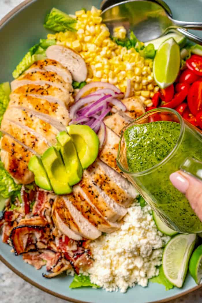 This Grilled Chicken Salad combines fresh corn, creamy avocado and juicy tomatoes with a zippy cilantro-lime vinaigrette for one tasty salad! Pouring cilantro lime vinaigrette onto grilled chicken salad