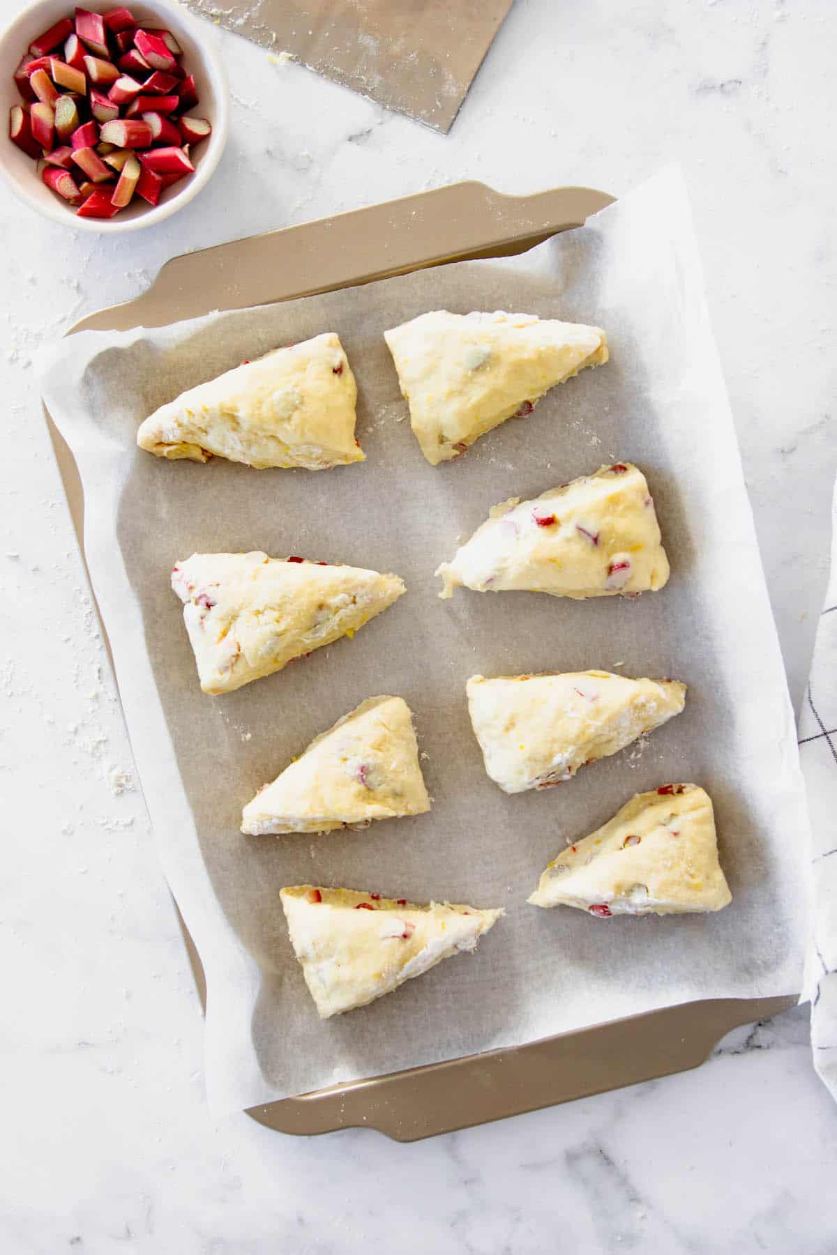 These rhubarb scones are moist inside and flaky outside, filled with juicy tart rhubarb and fresh lemon zest. Perfect with coffee or tea! Rhubarb scones on a baking sheet ready to go in the oven
