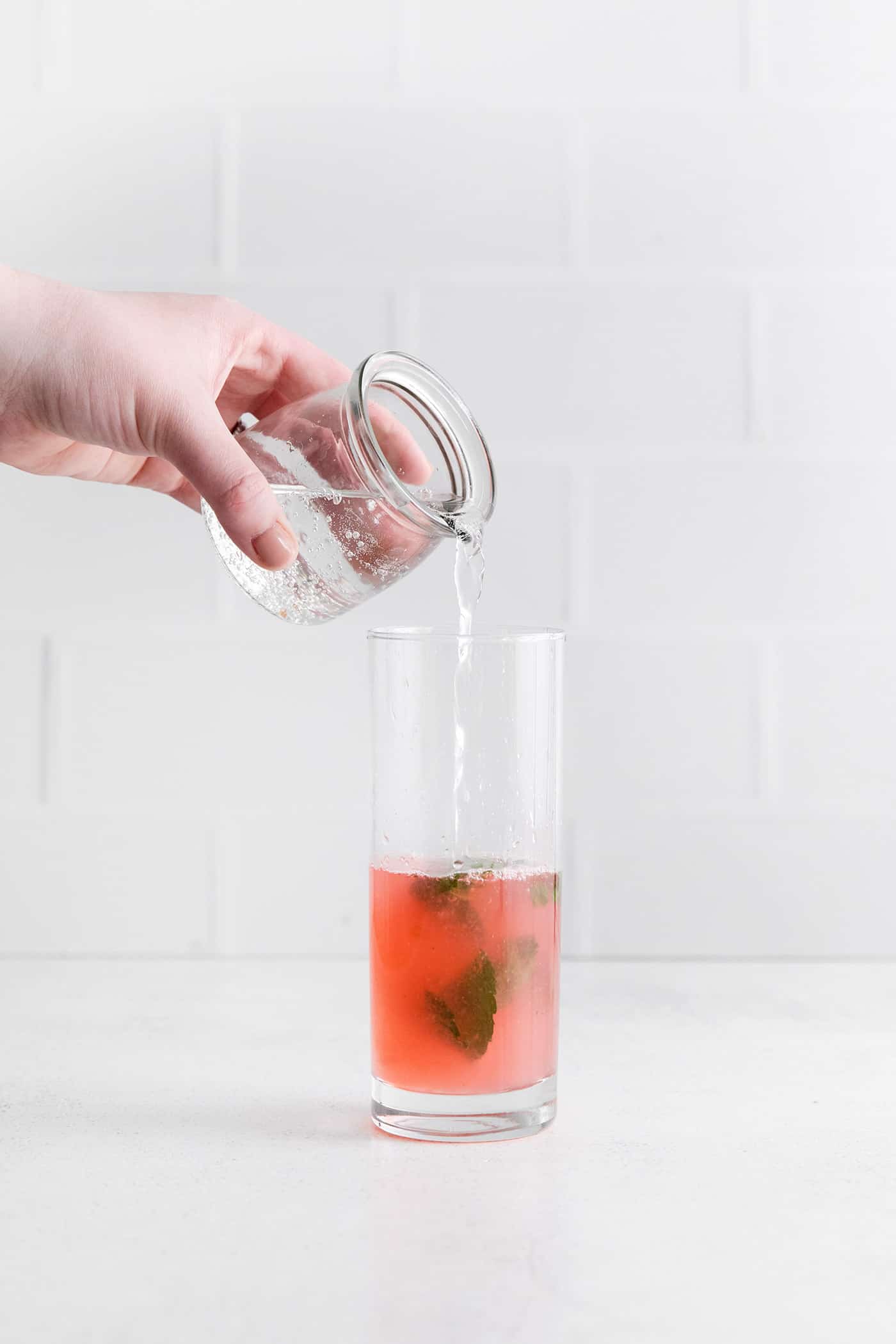 Relax by the pool this summer with a tall, cool Rhubarb Mojito. This twist on the classic cocktail is incredibly refreshing! Club soda being poured into a rhubarb mojito