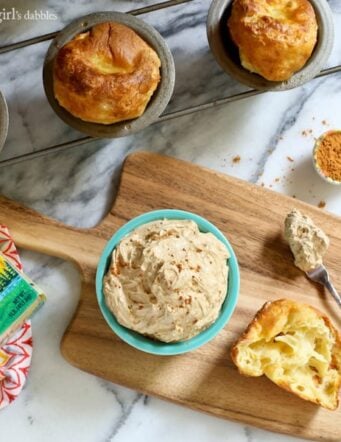 Overhead view of a bowl of pumpkin spiced butter on a wooden board, next to a batch of popovers.
