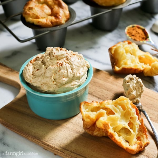 Creamy and luscious, this fluffy whipped pumpkin spiced butter is flavorful and lightly sweetened, bringing fall straight to your table! A bowl of pumpkin spiced butter on a wooden board, next to a batch of popovers.