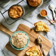 Overhead view of a bowl of pumpkin spiced butter on a wooden board, next to a batch of popovers.
