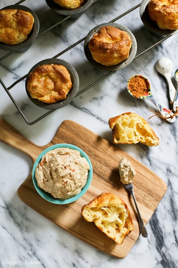 Creamy and luscious, this fluffy whipped pumpkin spiced butter is flavorful and lightly sweetened, bringing fall straight to your table! Overhead view of a bowl of pumpkin spiced butter on a wooden board, next to a batch of popovers.
