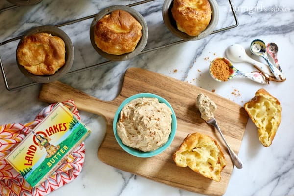 Creamy and luscious, this fluffy whipped pumpkin spiced butter is flavorful and lightly sweetened, bringing fall straight to your table! Overhead view of a bowl of pumpkin spiced butter on a wooden board, next to a batch of popovers.