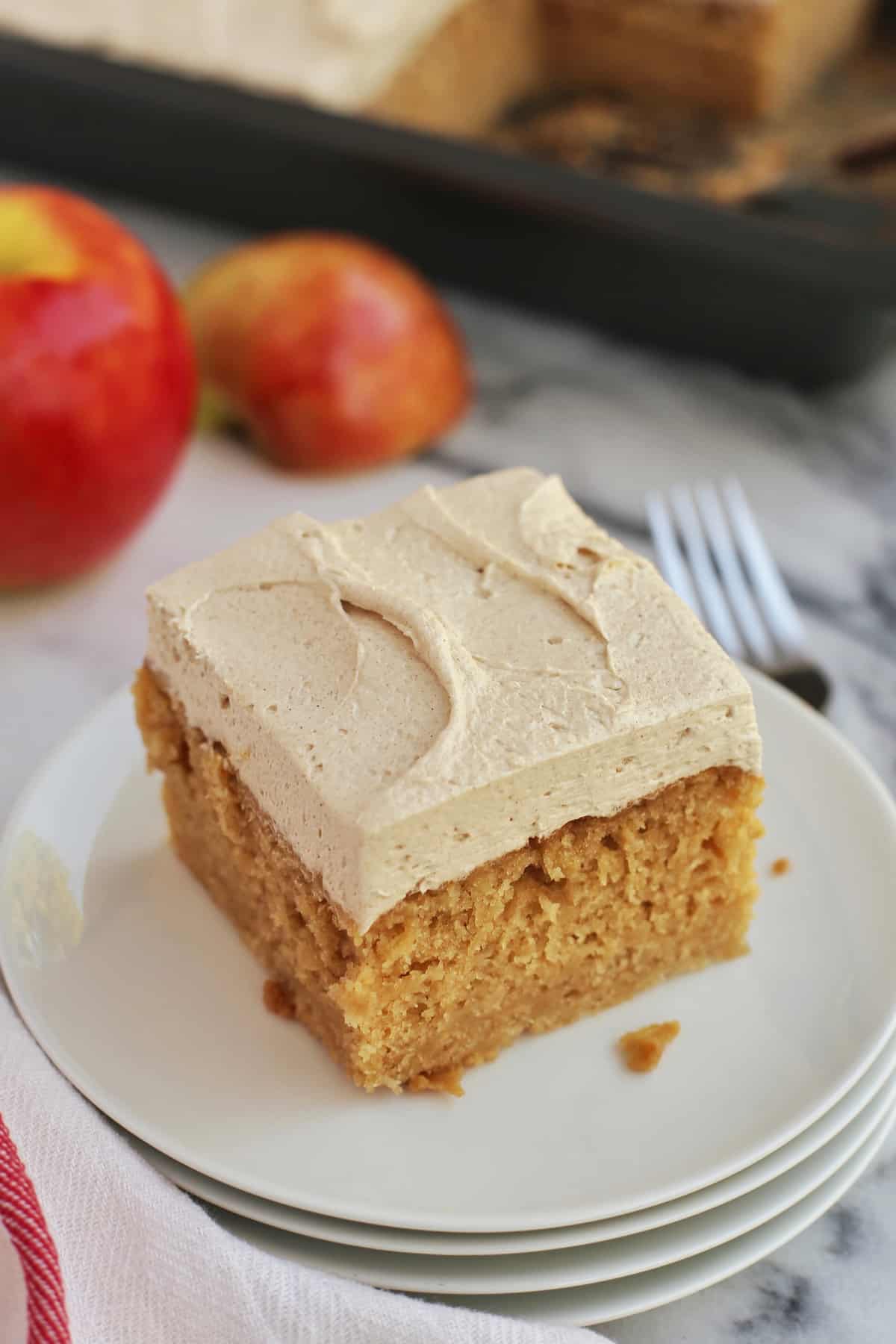 This easy apple cake is a moist, fluffy fall cake recipe filled with warm spice and fresh apples, frosted with brown sugar buttercream! A slice of frosted apple cake on a plate with fork
