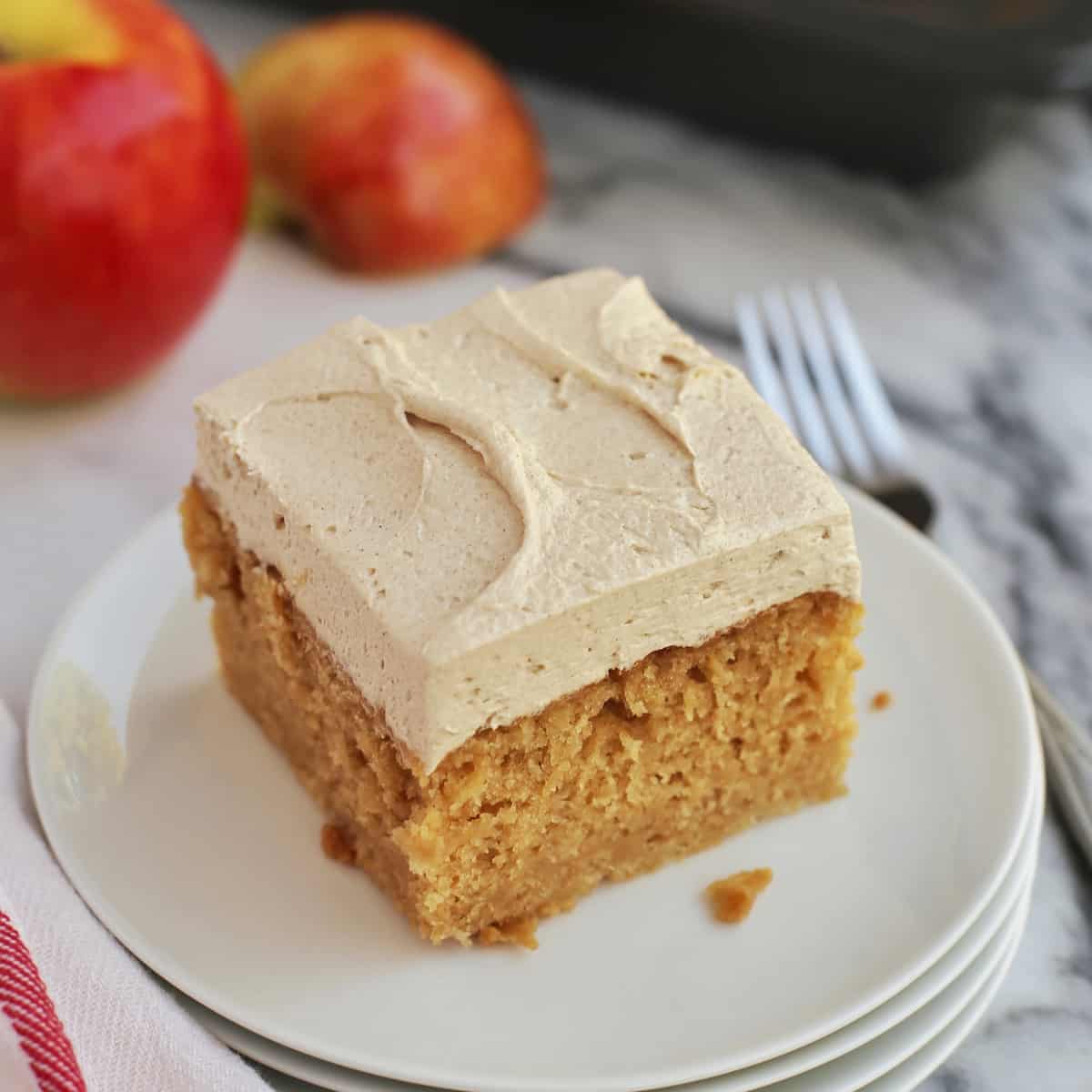 This easy apple cake is a moist, fluffy fall cake recipe filled with warm spice and fresh apples, frosted with brown sugar buttercream! A slice of frosted apple cake on a plate