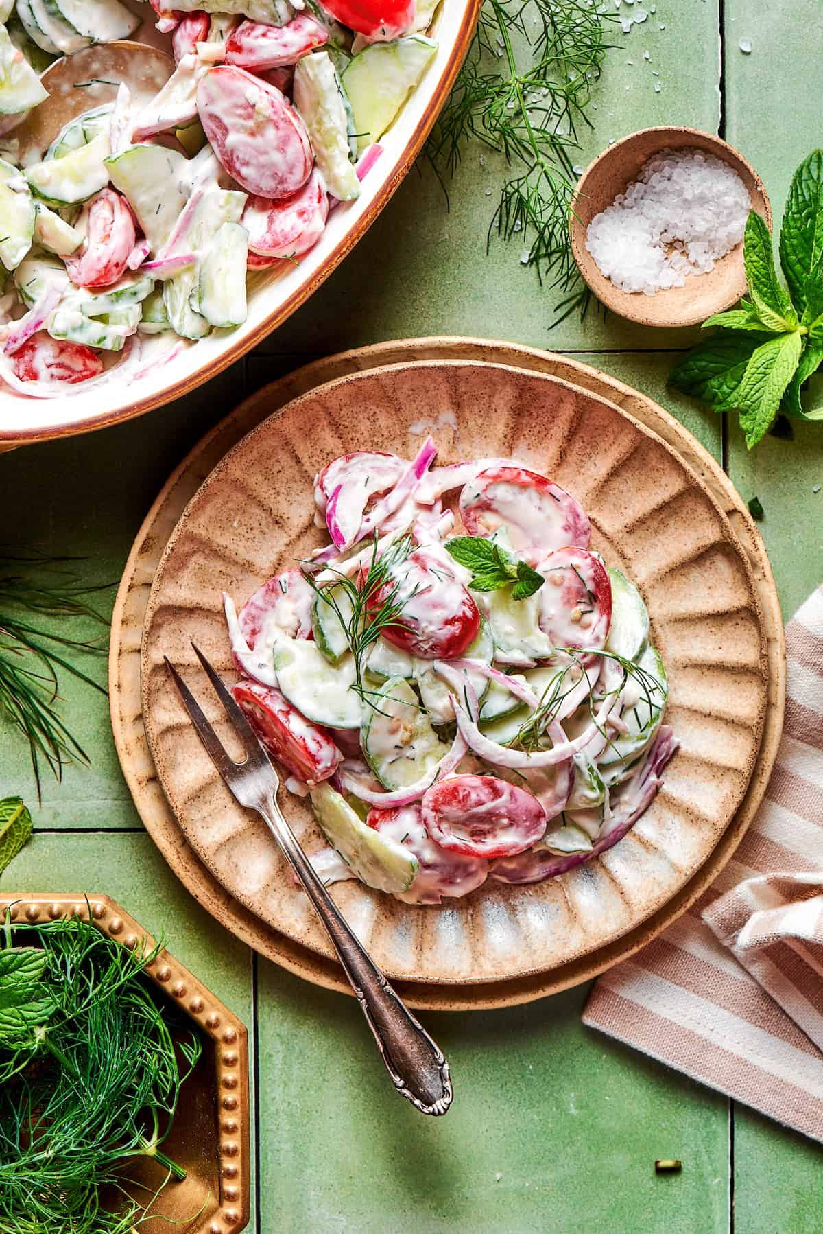 Creamy cucumber and tomato salad with fresh herbs on plate.