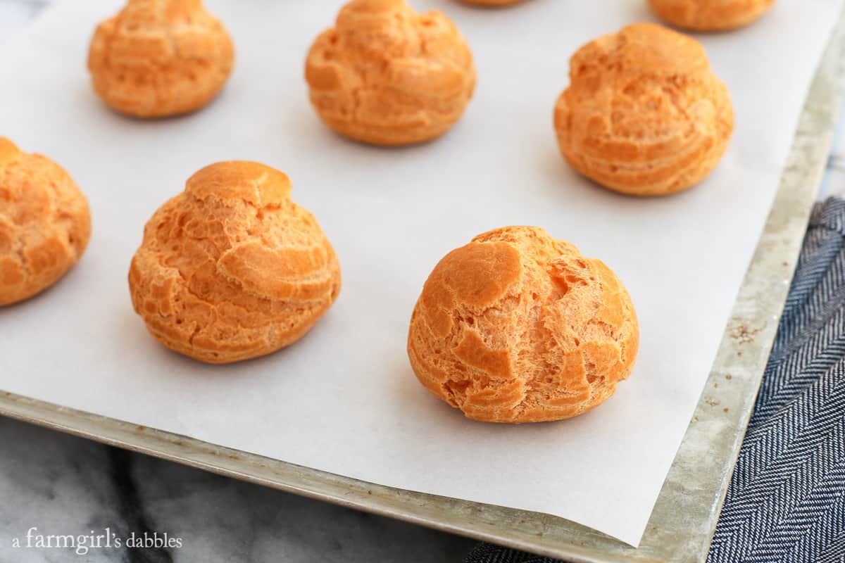 This pumpkin pie cream puff recipe is the perfect dessert for Thanksgiving. They're layered with pumpkin pie filling and maple whipped cream! Fresh baked Cream Puffs on a baking sheet.