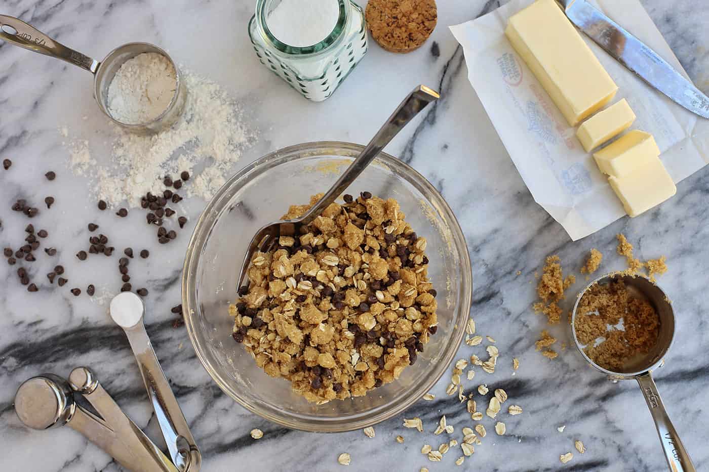 Super moist and perfectly spiced, this pumpkin muffins recipe features a crispy, buttery oat streusel dotted with melty chocolate chips. Oat and chocolate streusel in a bowl with a spoon, surrounded by streusel ingredients.