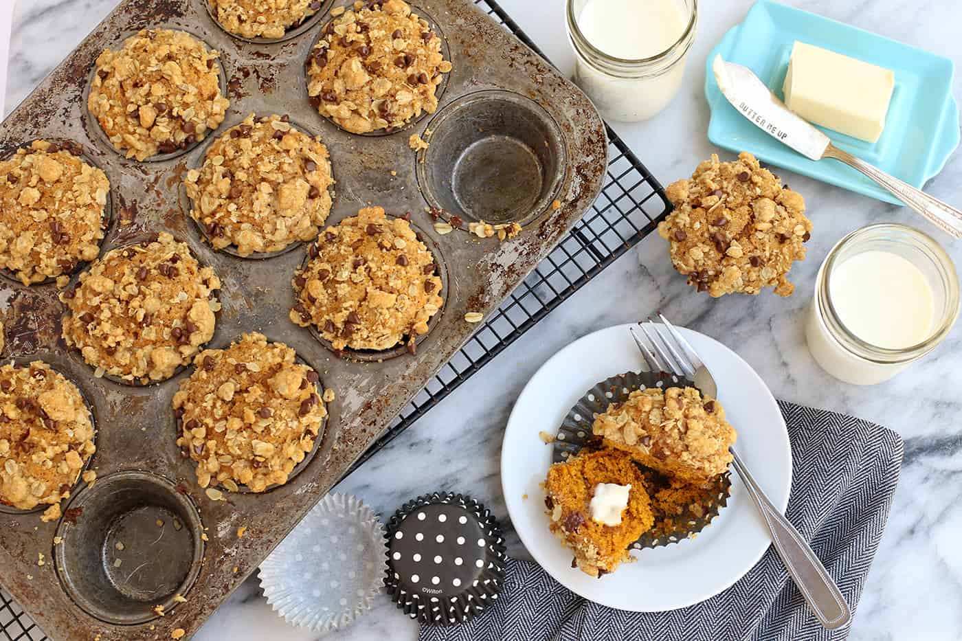 Super moist and perfectly spiced, this pumpkin muffins recipe features a crispy, buttery oat streusel dotted with melty chocolate chips. Overhead view of pumpkin muffins topped with streusel in a muffin tin next to one muffin cut in half on a plate.