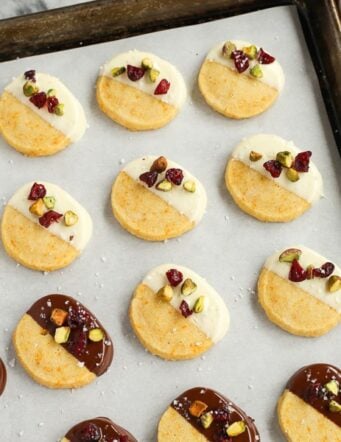 A sheet pan of shortbread cookies dipped in white and dark chocolate with cranberries and pistachios