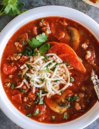 Overhead view of hearty pizza soup in a bowl topped with shredded mozzarella cheese.