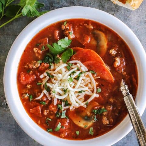 Overhead view of hearty pizza soup in a bowl topped with shredded mozzarella cheese.