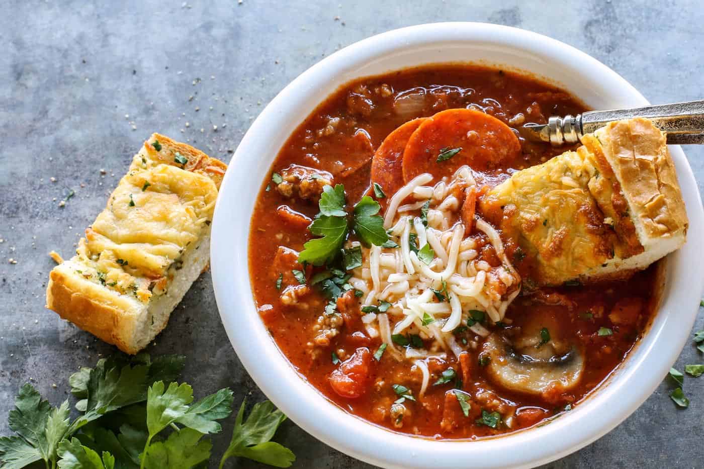 A piece of garlic bread partially dunked into a bowl of pizza soup.