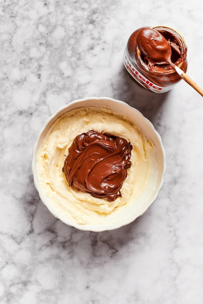 These Nutella cheesecake bars top a fudgy brownie base with creamy Nutella cheesecake for a rich, decadent dessert that’s surprisingly easy! Nutella added to cheesecake mixture in bowl.
