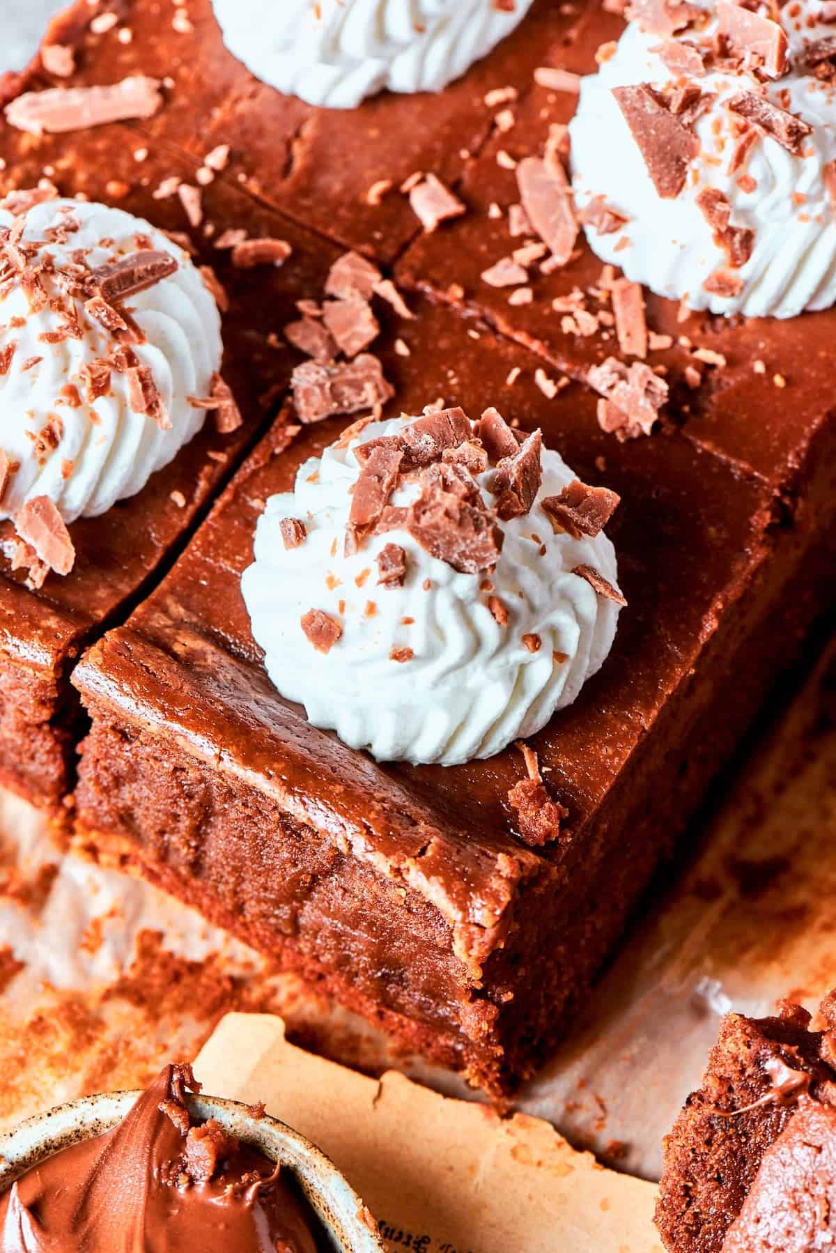 These Nutella cheesecake bars top a fudgy brownie base with creamy Nutella cheesecake for a rich, decadent dessert that’s surprisingly easy! Sliced Nutella cheesecake bars topped with whipped cream and chocolate shavings.