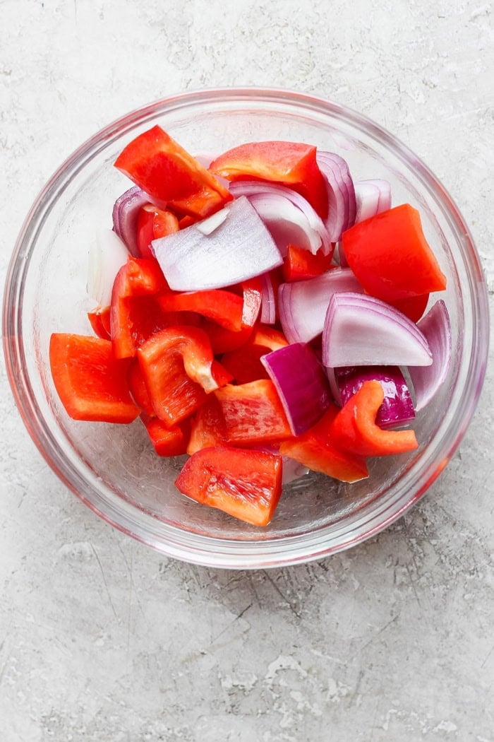 Grilled Hawaiian chicken kabobs have the perfect balance of heat and sweet, with pineapple, red pepper, red onions and savory bacon. Yum! Overhead view of red bell pepper and red onion pieces in glass bowl