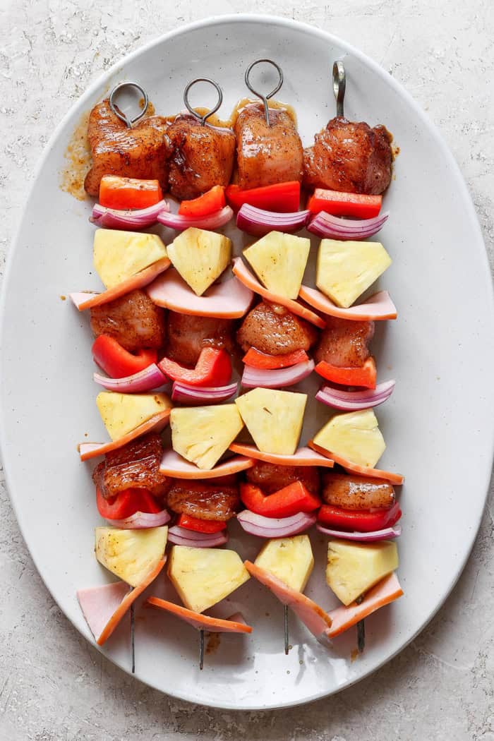 Grilled Hawaiian chicken kabobs have the perfect balance of heat and sweet, with pineapple, red pepper, red onions and savory bacon. Yum! Overhead view of Hawaiian chicken chili kabobs on platter before grilling