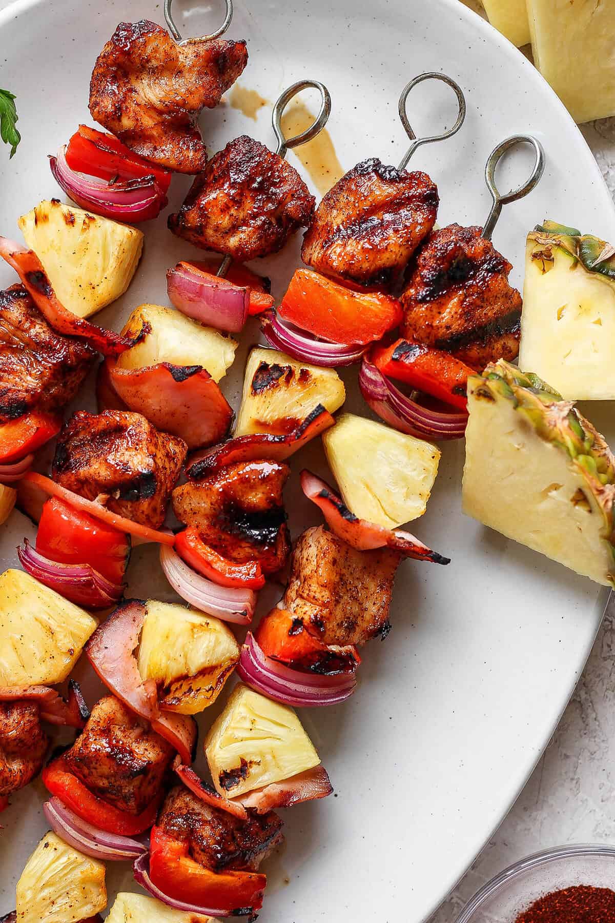 Grilled Hawaiian chicken kabobs have the perfect balance of heat and sweet, with pineapple, red pepper, red onions and savory bacon. Yum! Overhead view of grilled Hawaiian chicken chili kabobs on platter