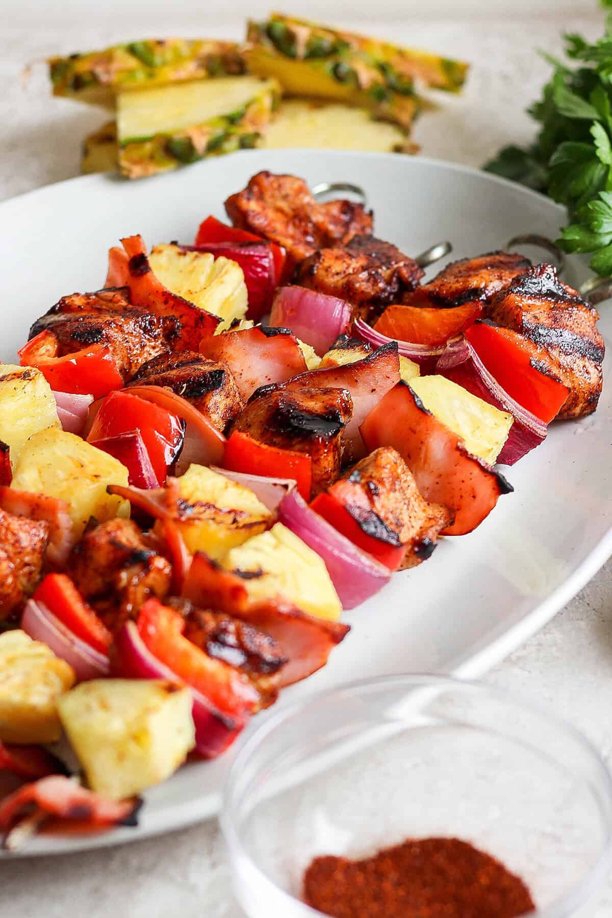 Grilled Hawaiian chicken kabobs have the perfect balance of heat and sweet, with pineapple, red pepper, red onions and savory bacon. Yum! Platter of grilled Hawaiian chicken kabobs