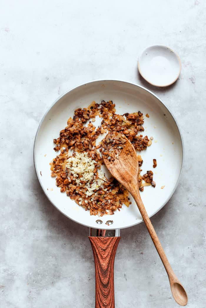 These easy Cheesy Stuffed Mushrooms are an irresistible appetizer or side dish, with lots of melty cheese and garlicky breadcrumbs. Yum! Overhead view of mushroom stems, onion, and garlic in pan